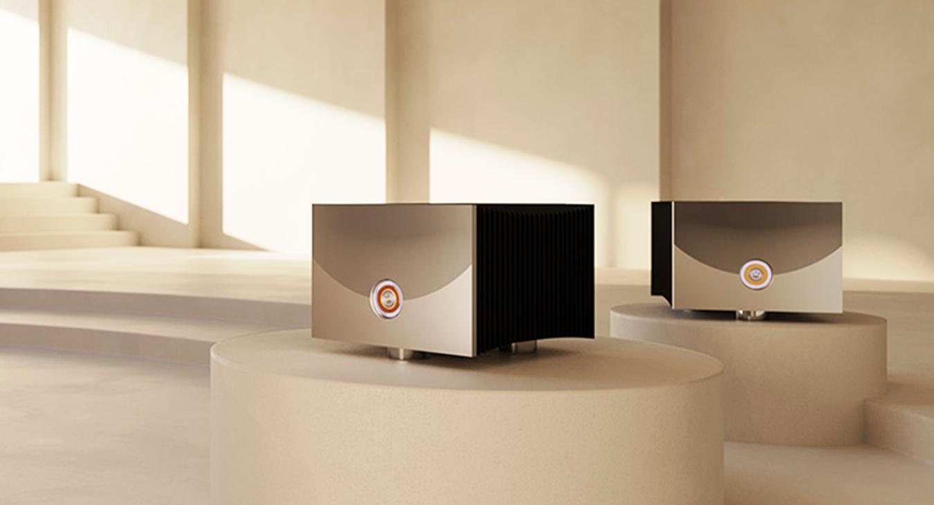 A pair of Linn Klimax Solo 800 Power Amplifiers.  Each on a plinth in a light coloured large room with light streaming from the left