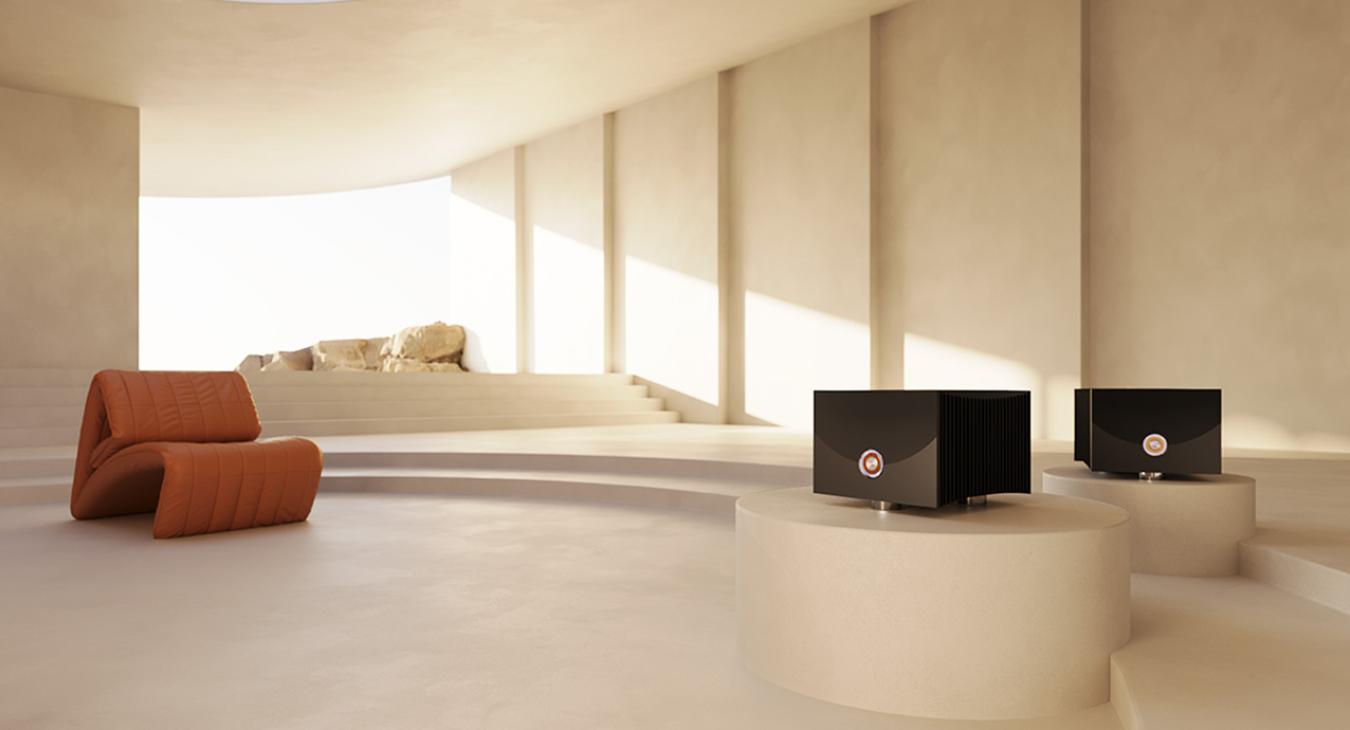 A pair of black Linn Klimax Solo 800 Power Amplifiers in silver on a plinth in a large light coloured space with a red chair to the right.